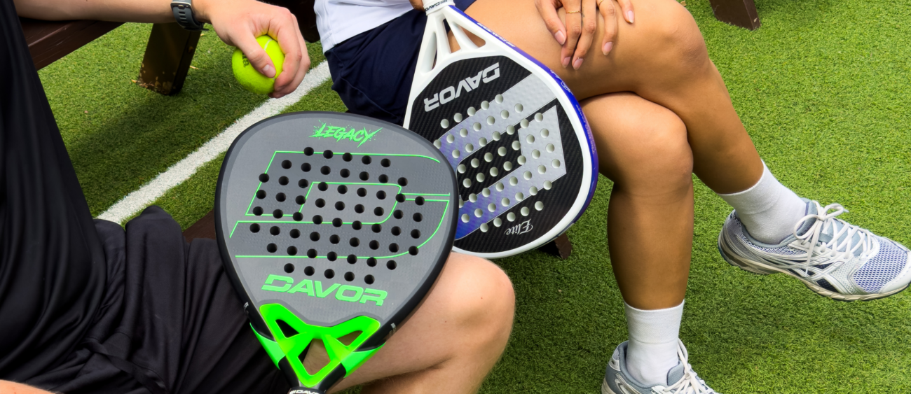 Davor Legacy green and Elite padel racquets resting on players' laps courtside, with a padel ball visible in hand